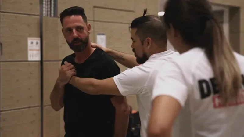 Instructeur demonstreert een verdedigingstechniek tijdens een Krav Maga-les, terwijl een deelneemster toekijkt